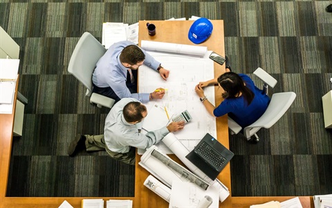 Three people go over planning diagrams at a desk