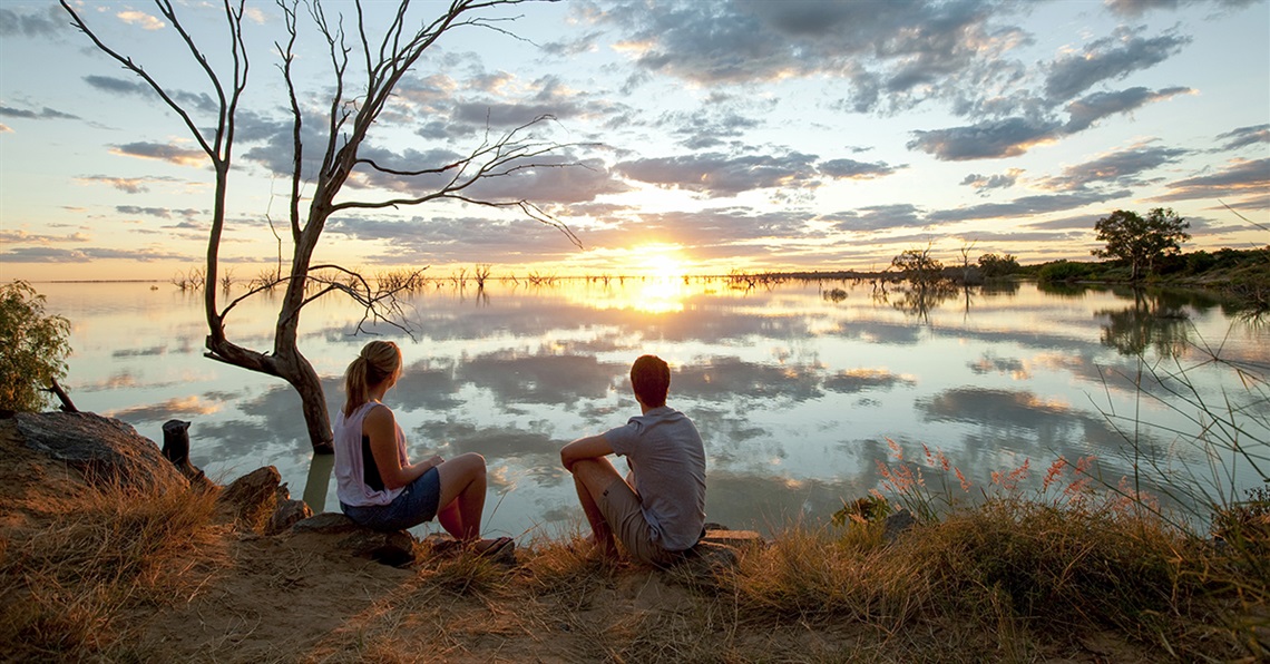 A young couple sits on the bank of Lake Menindee watching the sun set