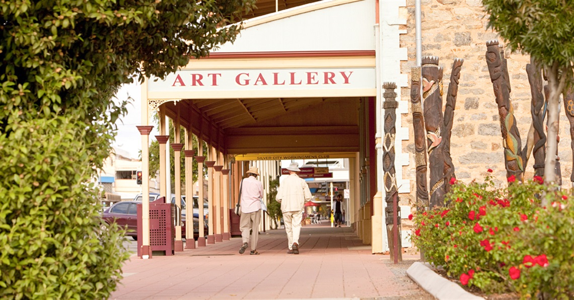 Two people walking along the footpath in front of the Broken Hill Regional Art Gallery.