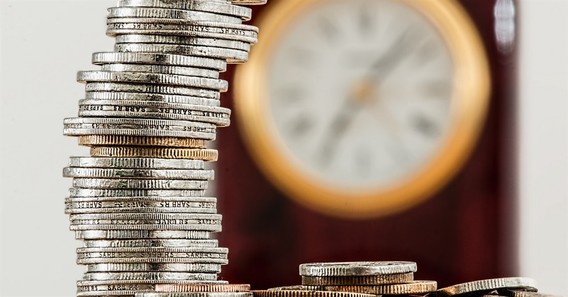A stack of coins in front of an out of focus clock