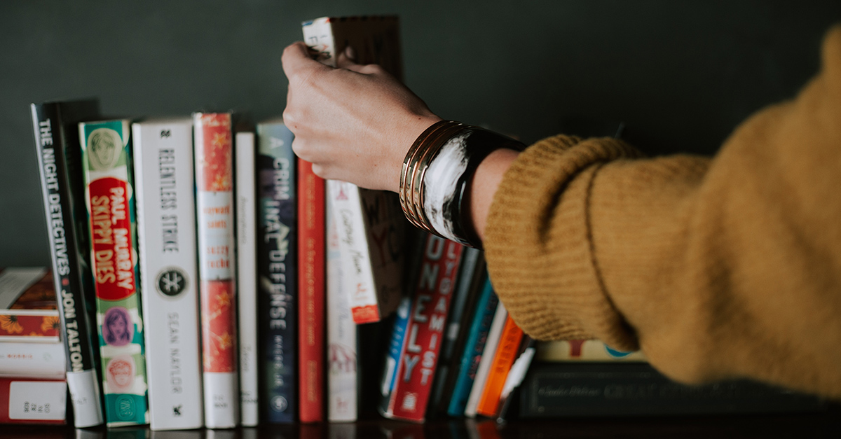 Persons hand picking a book from a shelf