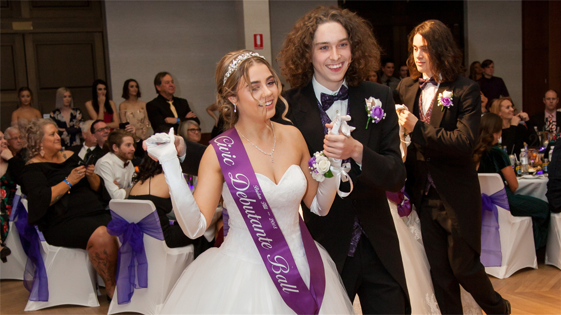 image of a girl and boy dancing at a debutante ball, surrounded by smiling people sitting at their tables watching them