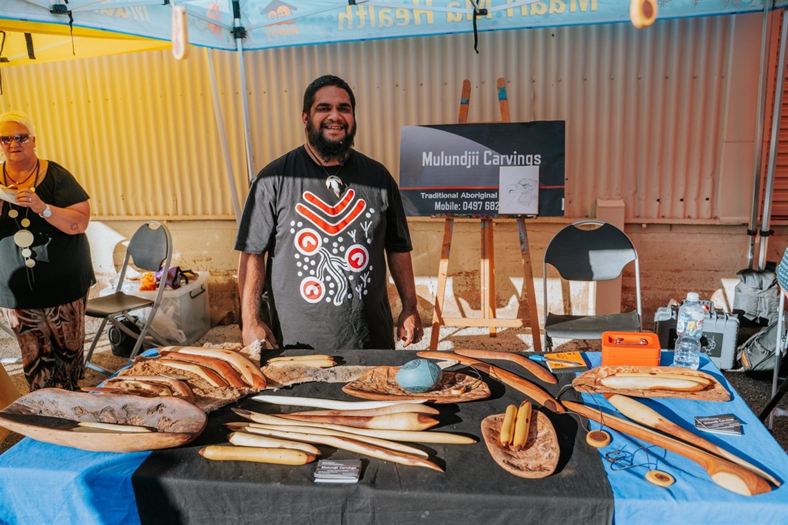 Image of Aboriginal market Stall with hand made objects for sale on a table and local Aboriginal Artist Anthony hayward smiling towards camera.jpg