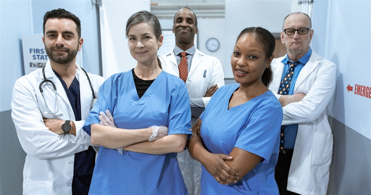 image of four medical professional wearing hospital clothing standing in a row with their arms crossed cropped at the bottom