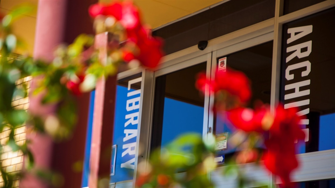 Image of front glass dorrs of the Library and Archives with red flowers in the front of the shot