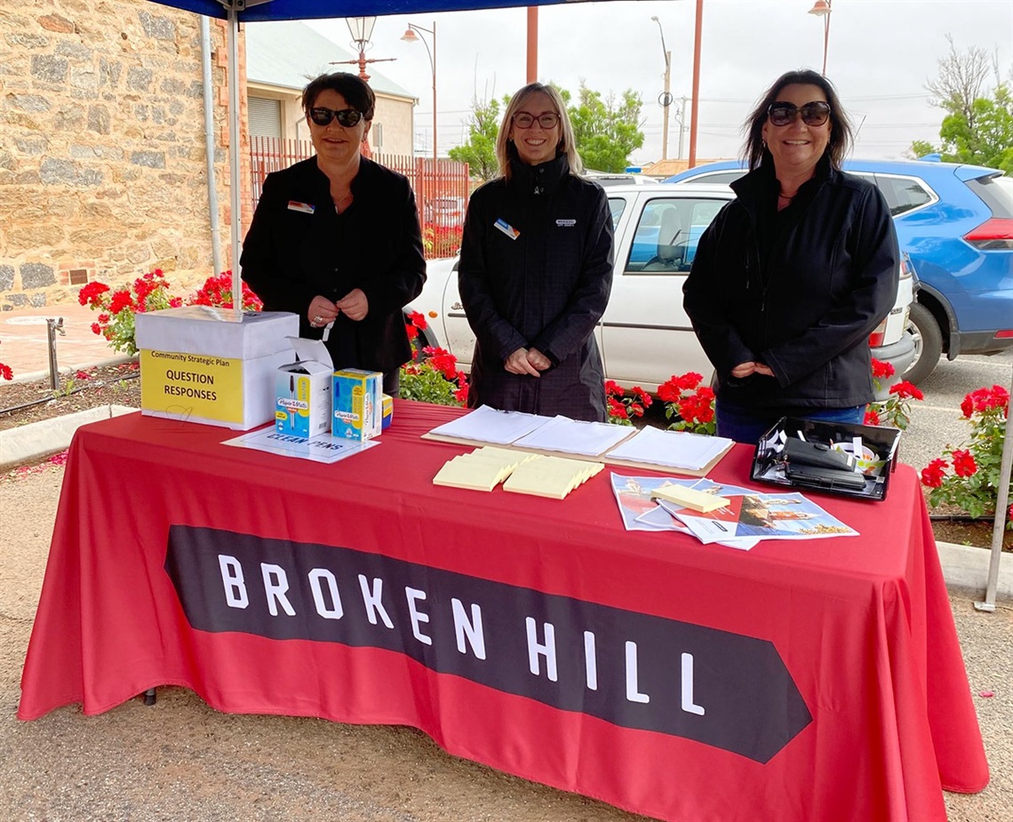 Three female council employees, standing behind a table at a local community consultation session.jpg