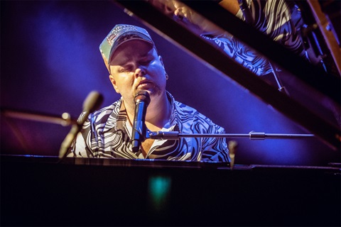 Musician Brad Cox singing in with a microphone while playing the piano