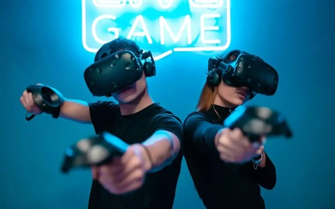 male and female gamers with VR headset on holding gaming controllers and pointing at the screen