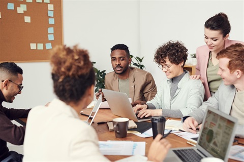 image of a group of multicultural individuals overlooking paperwork and computers on a desk.