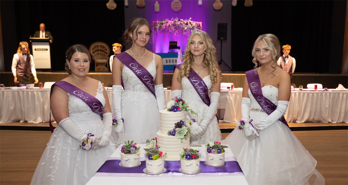 Image of four debutantes standing in front of one large white cake and four smaller ones smiling at the camera.