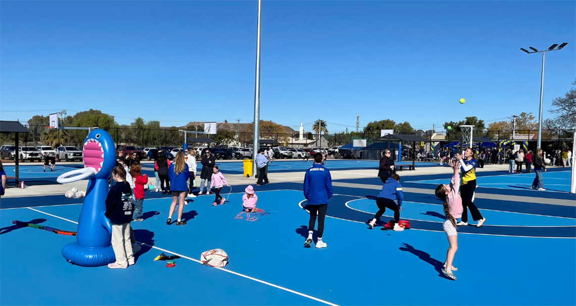 Image of blue softfall netball courts, with various aged children playing exhibition matches on them