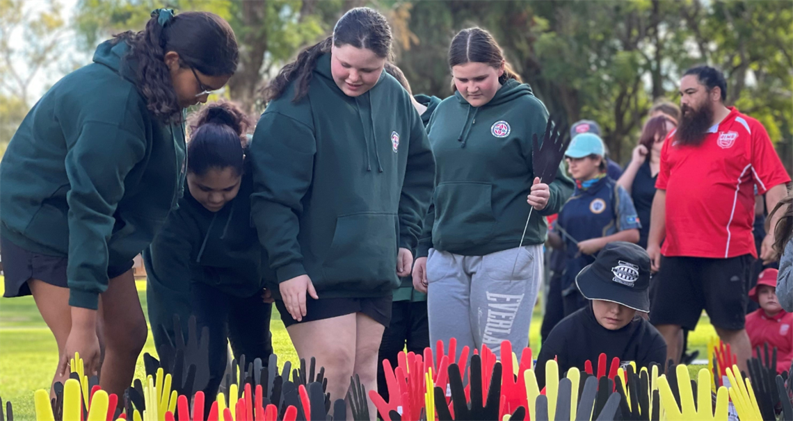 Reconciliation week sea of hands activity showing high school students placing red, yellow and black hands into the ground