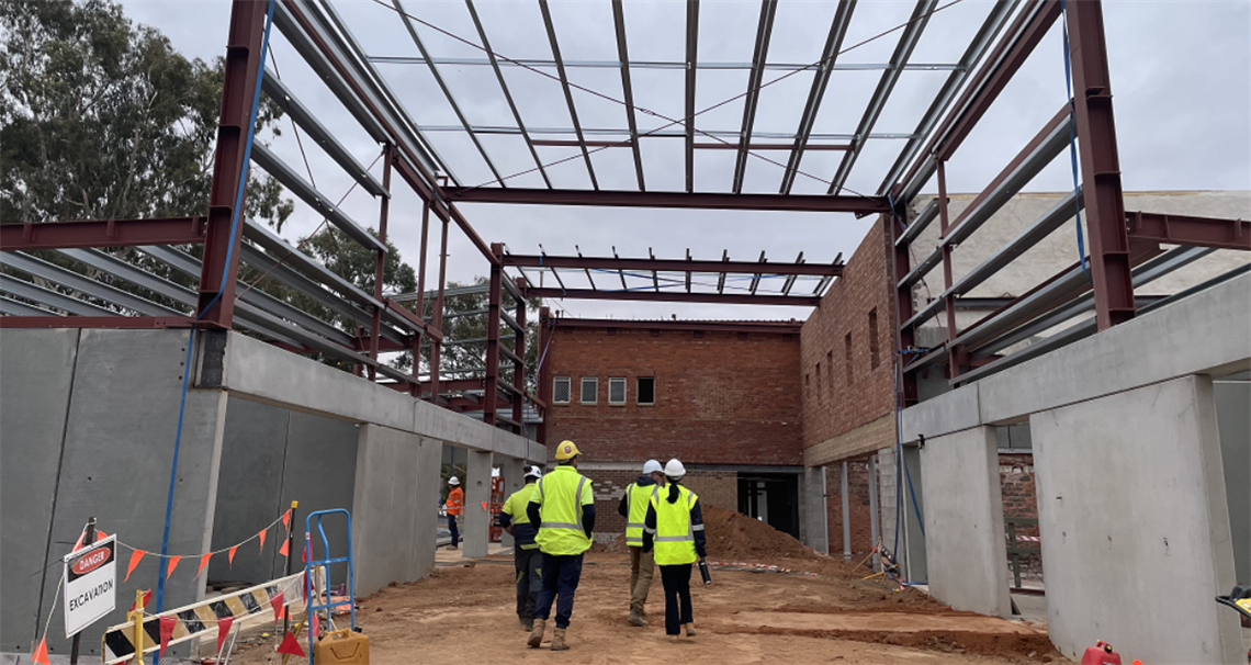 two engineers wearing high visibility vests looking up at a large steel frame on a construction site