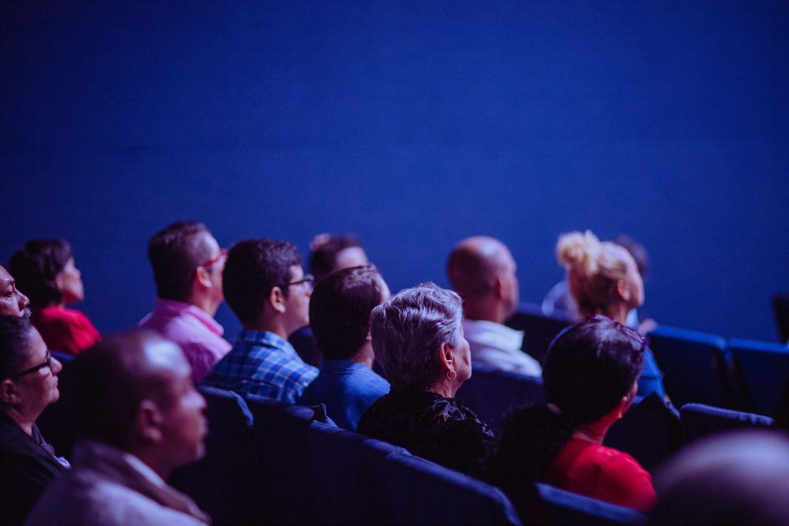 blue background with a crowd of people sitting in chairs with their heads facing he front of the room