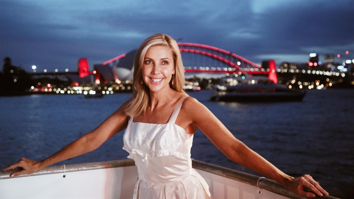 Catriona Rowntree standing with her arms out wise and you can see Sydney Harbour bridge in the background