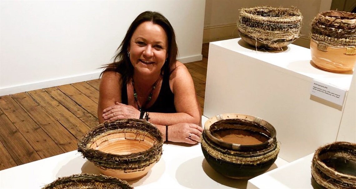 image of kathryn graham leaning on a white gallery plinth next to her weaved backsets