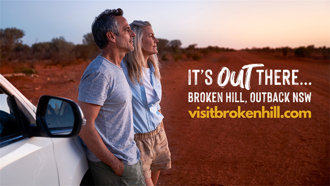 man and woman leaning against a car looking at desert sky text on image says its out there broken hill and it is written above the website url visitbrokenhillcom