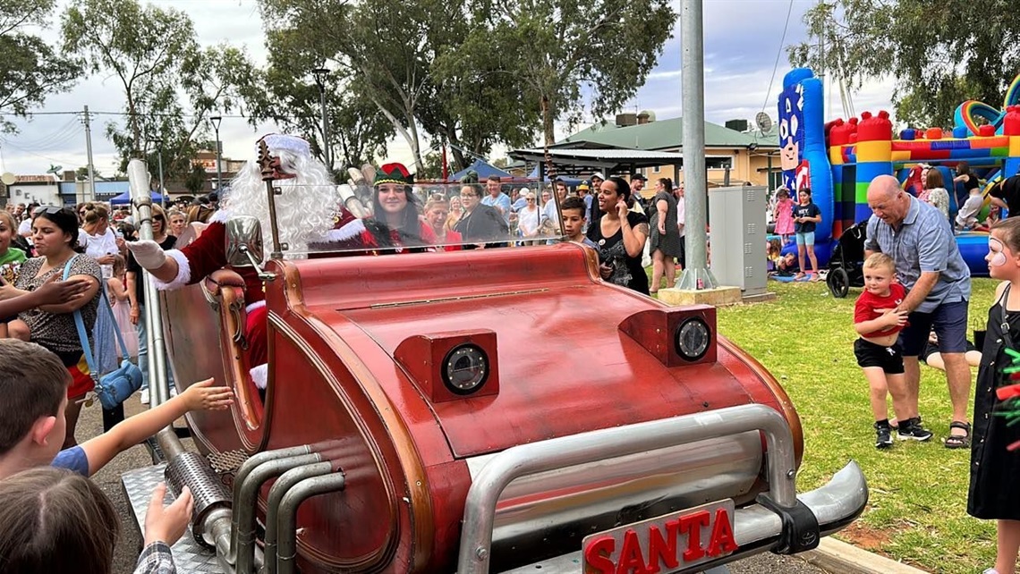red santas sleigh car with santa inside waving to a crowd at a community christmas event