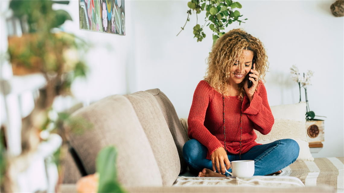 woman sitting on a couch with a cup of coffee talking on her phone