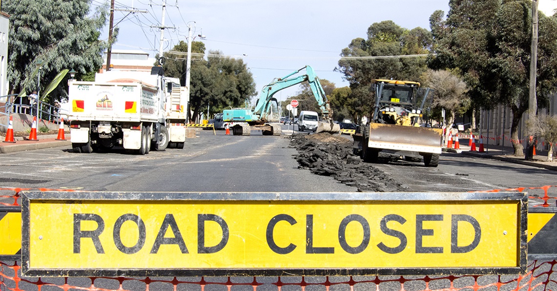 A road closed sign blocks off a road while heavy machinery conducts roadworks